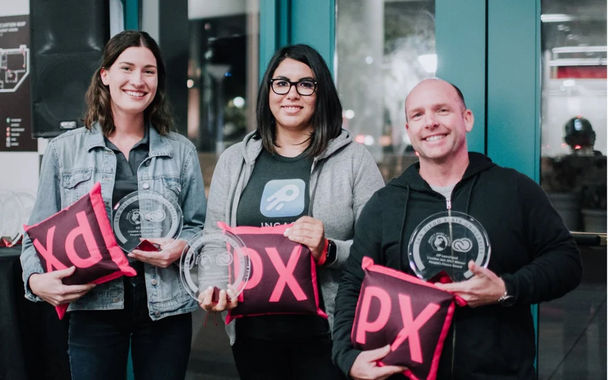 Three team members holding Creative Jam trophies and Adobe XD pillows.