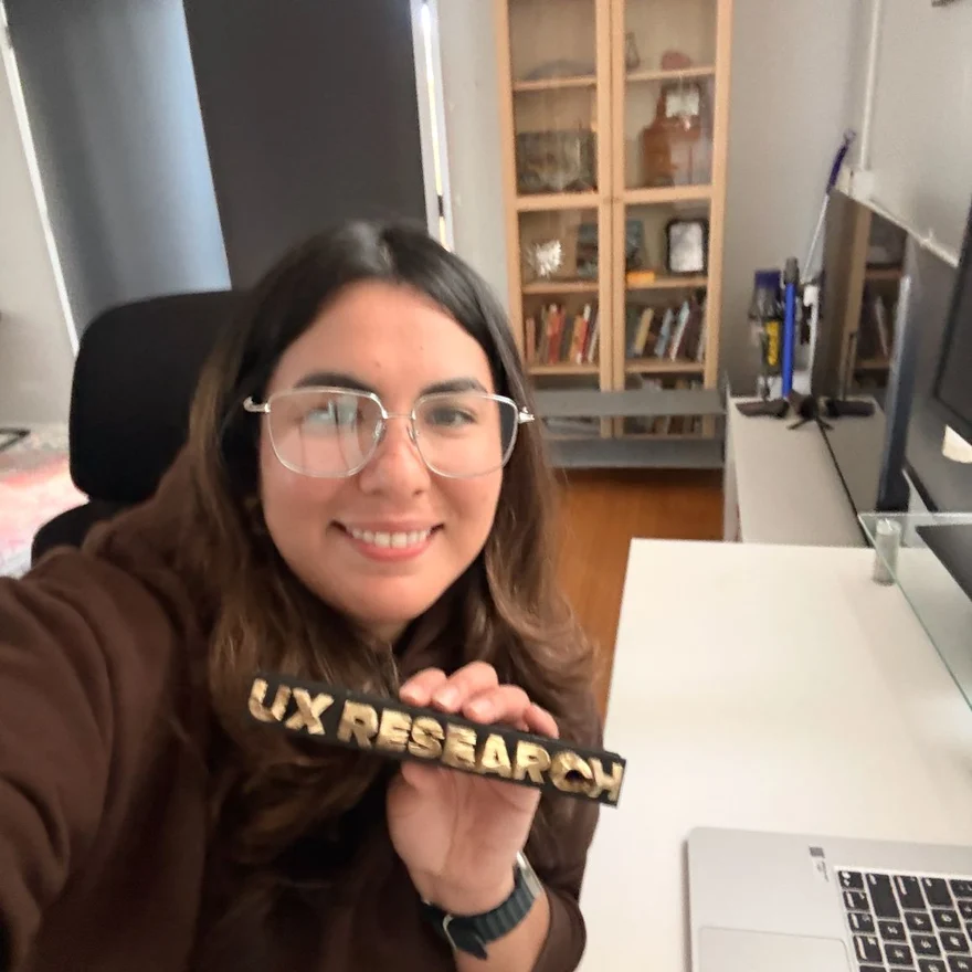 Thania at her desk, smiling and holding a black and gold UX Research award.